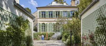 Historic building with large windows, light facade, lush garden, and paved pathway on a sunny day.