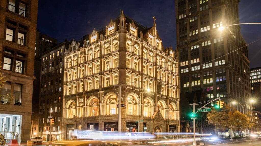 Historic building with ornate architecture illuminated at night at a busy city intersection.