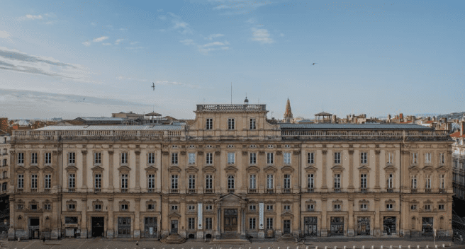 Large historic building with ornate facade, numerous windows, central entrance, and blue sky background