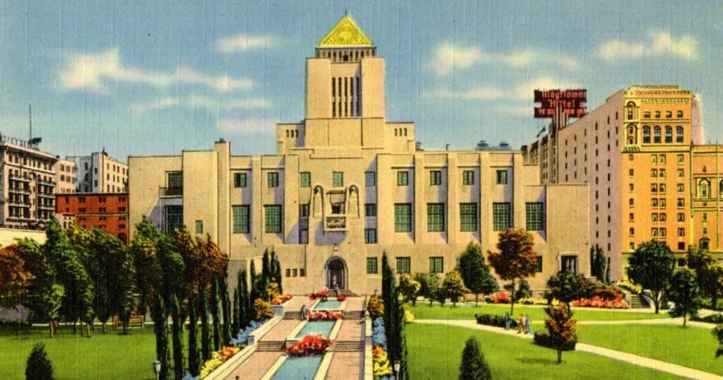 A historic building with a pyramidal roof, gardens, fountains, and surrounding urban structures.
