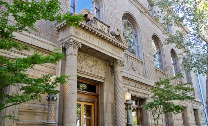Historic City Library's ornate façade with arched windows, columns, carvings, and surrounding trees.