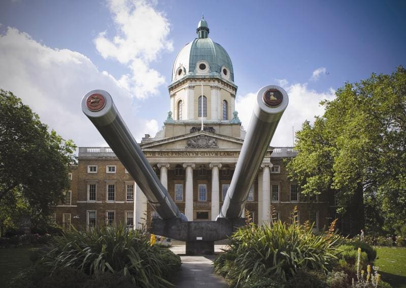 Historic building with a dome, neoclassical architecture, and two large naval guns in the foreground.