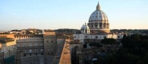 Historic building complex with a dome, classical architecture, cityscape background, sunset lighting.