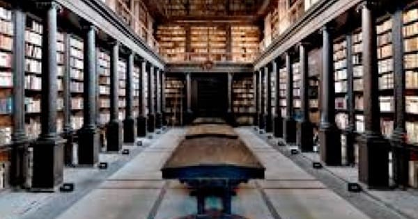 Spacious historic library with tall shelves, high ceiling, ornate decorations, and central tables.