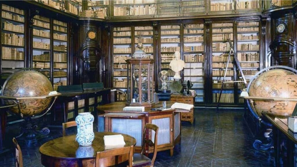 Historic library with wooden furniture, bookshelves, globes, scientific instruments, and artifacts.