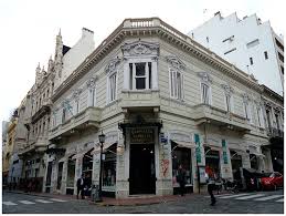 Historic ornate building on a street corner with commercial establishments, people nearby.