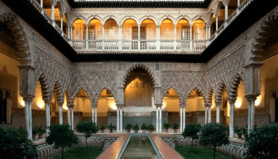 Interior courtyard of a historic palace with arches, carvings, central water feature, and greenery