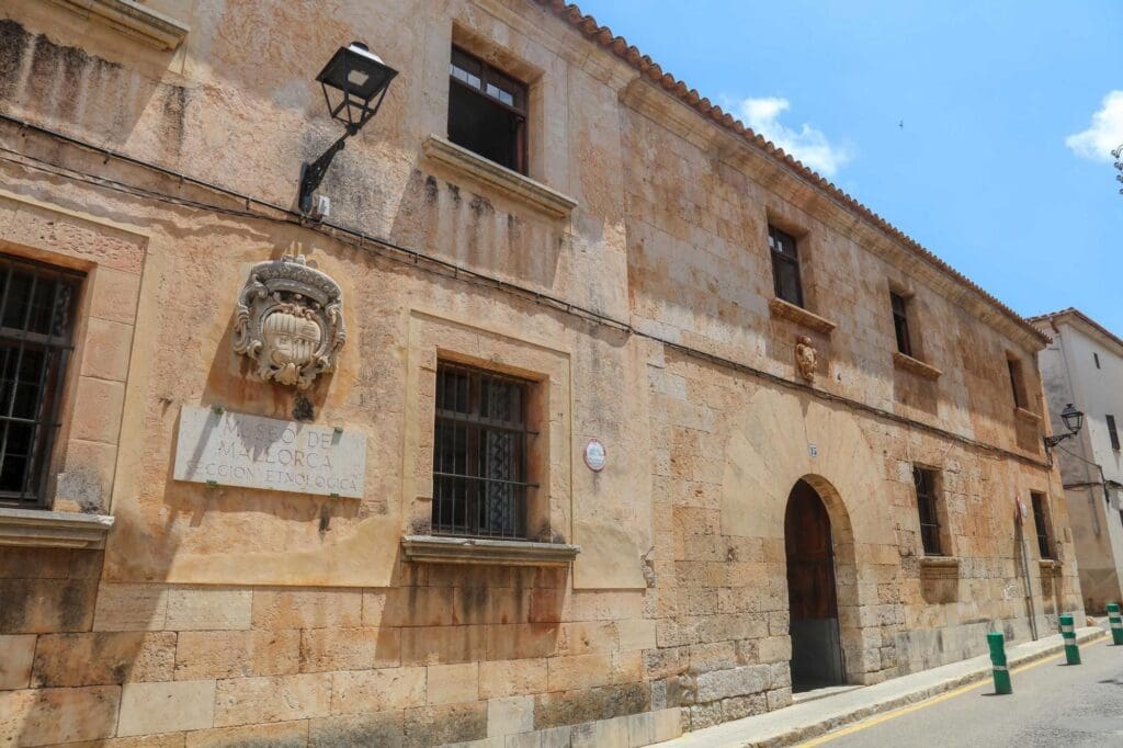 Historic stone building with Museo de Mallorca, Sección Etnológica sign, emblem, windows, and arched doorway.