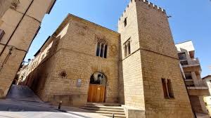 A historic stone building with a tower, arched doorways, and high narrow windows on a paved street.