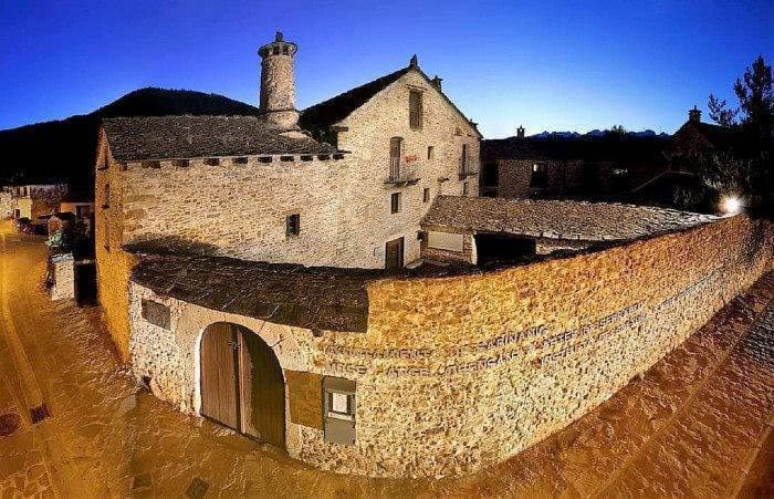 Historic stone building with large arched door, windows, chimney, and a twilight sky background.