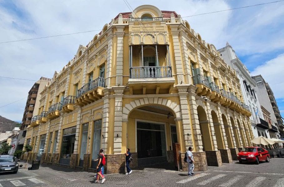 Historic yellow building with balconies and arched windows at a street corner, people walking nearby.