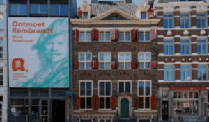 Street view of a historical brick building with red shutters and Rembrandt exhibition advertisement.