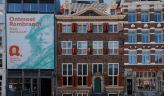 Street view of a historical brick building with red shutters and Rembrandt exhibition advertisement.