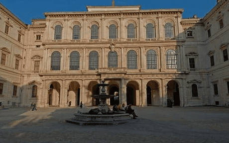 Historical building with arched windows and columns surrounding a courtyard with a central fountain.