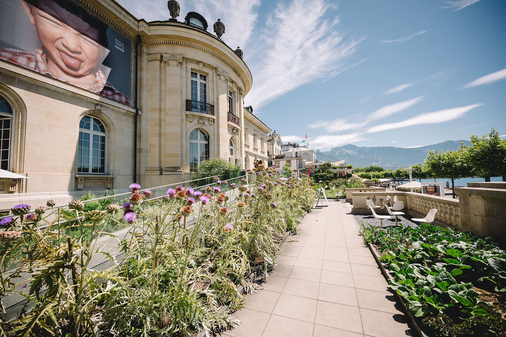 Historical building with classical architecture, flowering courtyard, mountains and clear blue sky.