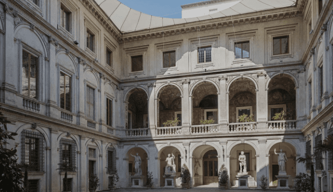 Historical building with a courtyard, two-story colonnade, arched openings, statues, balcony, and windows.
