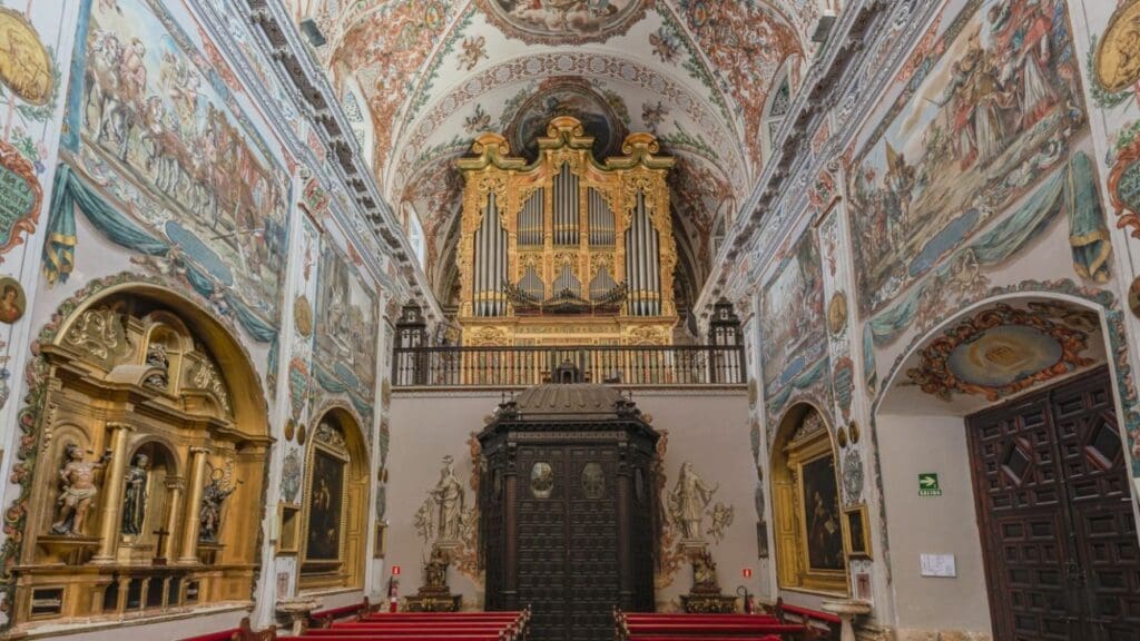 Elaborately decorated historical church interior with an ornate pipe organ, frescoes, and red pews.