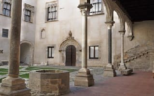 historical courtyard with stone well, columns, arches, windows, arched doorway, and stone steps