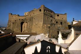 Large historical stone fortress with arched windows, surrounded by white-roofed buildings.