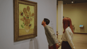 Two people holding hands, closely observing a painting of sunflowers in an art gallery.