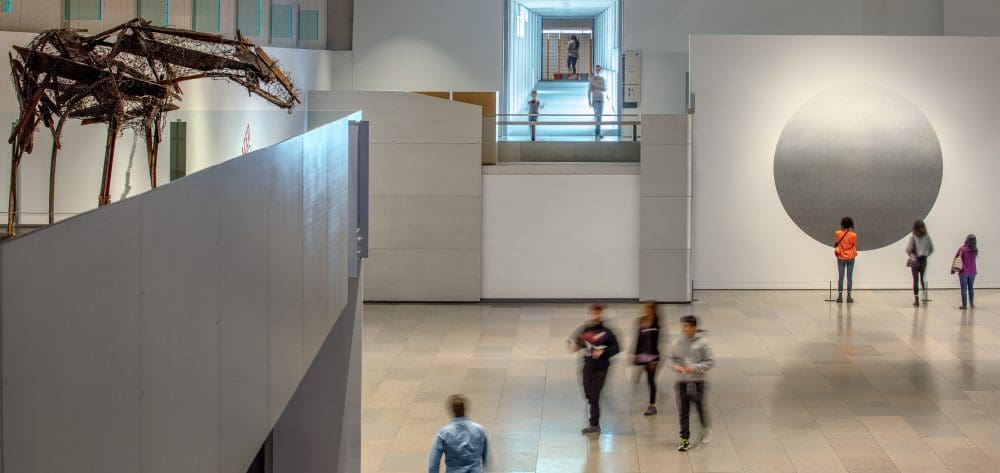 Indoor art gallery with a metallic animal sculpture and a circular artwork on the wall.
