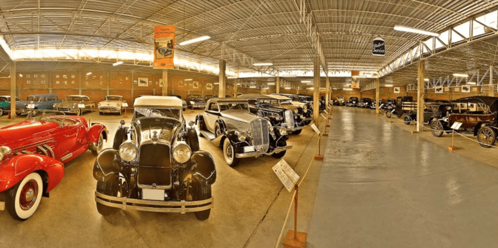 Indoor exhibition of vintage and classic automobiles with placards in a spacious, well-lit setting.