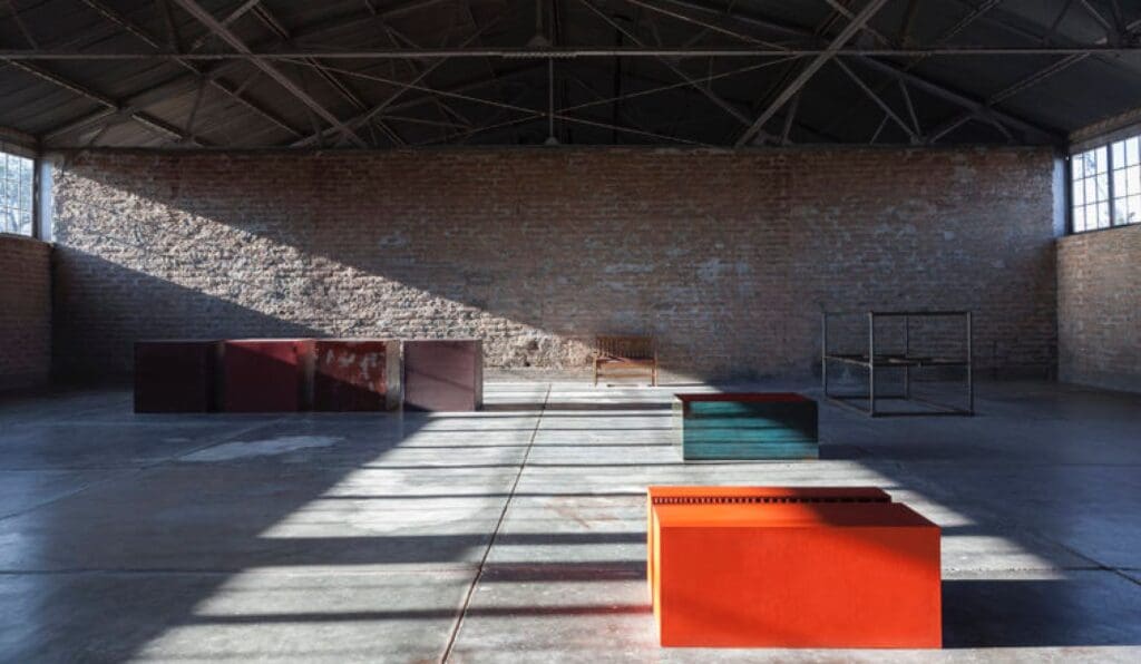 Industrial room with brick walls, steel-beamed roof, and various colored blocks on a concrete floor.