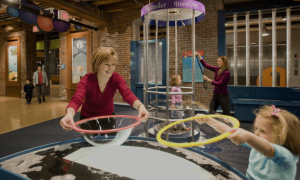 People creating bubbles with circular tools at an interactive museum exhibit with educational displays.