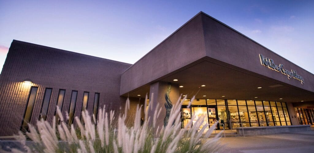 Modern building labeled Kitty Bear Canyon Library, with large glass windows and decorative grasses.