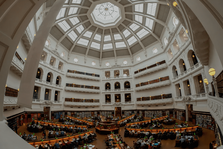 A wide interior of a large, domed library with arched windows, study tables, and bookshelves.