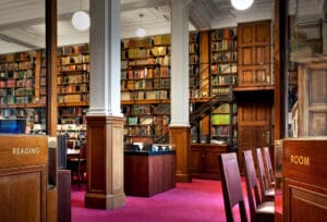 Large, well-lit library reading room with bookshelves, wooden decor, and tables for study.