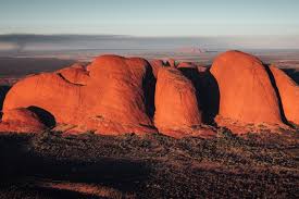 Large red rock formations in an arid landscape with sparse vegetation and a clear sky.