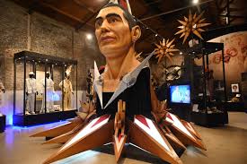 Large sculpture of a head with a headdress, surrounded by artifacts in a museum exhibit.