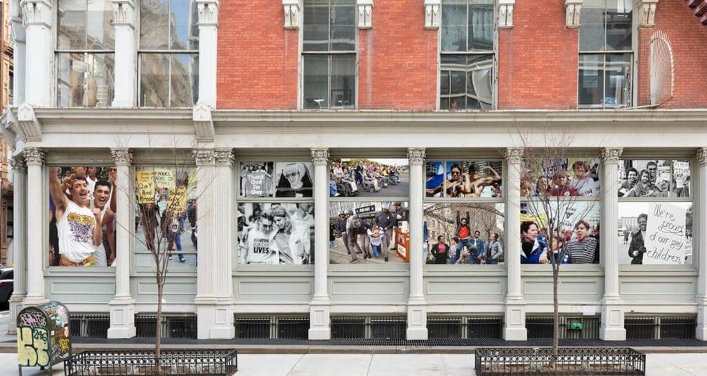 Building facade with large photographs depicting LGBTQ+ activism, graffiti-covered mailbox in foreground