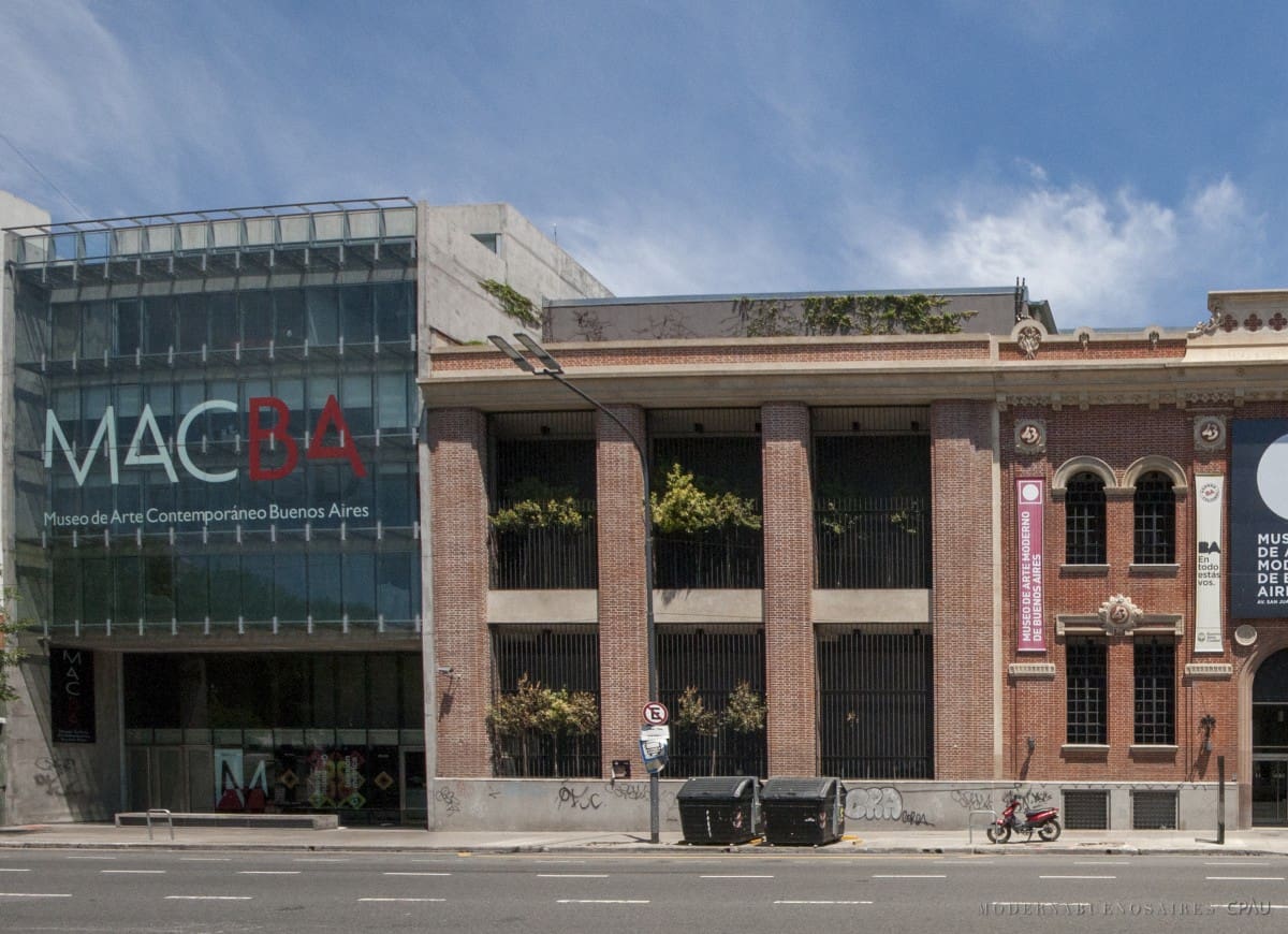 Exterior view of MACBA and neighboring building, with trash bins and a motorcycle on the street.