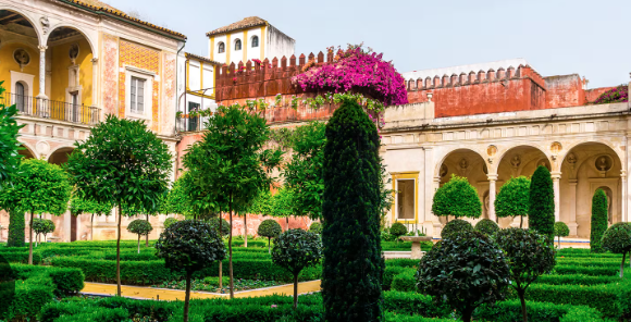 Well-manicured garden with geometric hedges, topiary trees, bougainvillea, and arched walkway architecture.