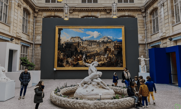 Group at marble sculpture in courtyard with classical buildings, framed cityscape painting, and artworks.