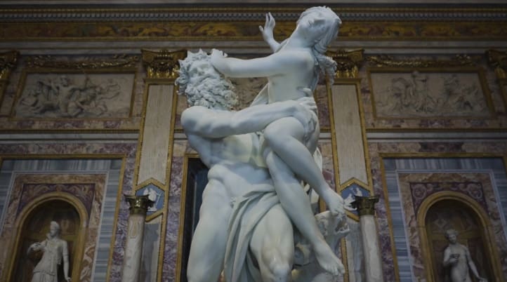 Marble sculpture of two figures in a dynamic pose, with an ornate architectural background.