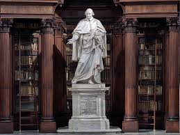 Marble statue in the center of an ornate library with wooden bookshelves and carved columns in the background.