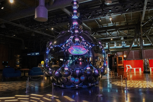 Metallic spherical structure made of smaller spheres with colorful lights in an industrial-style room