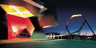 Modern architectural structure with angular designs, bright lighting, and a large ring sculpture.