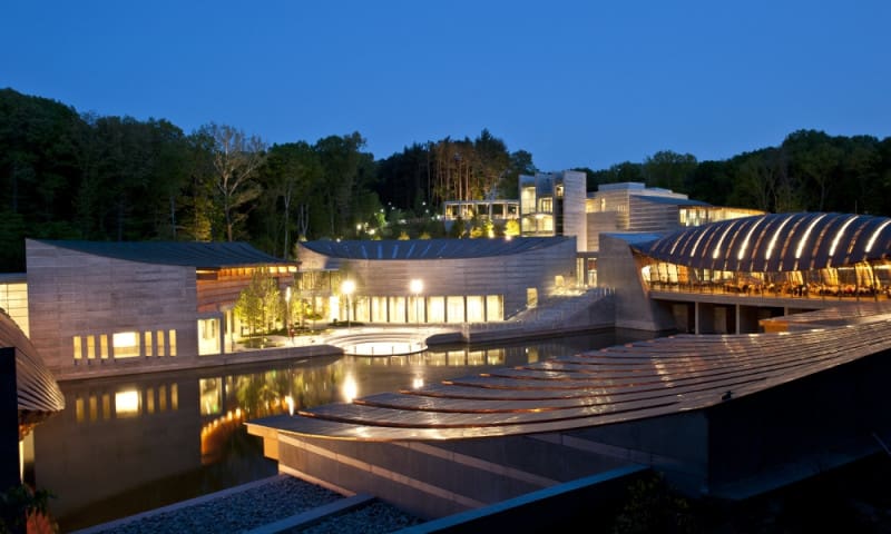 Modern architectural complex with curved, angular designs, water features, and landscaped areas at night