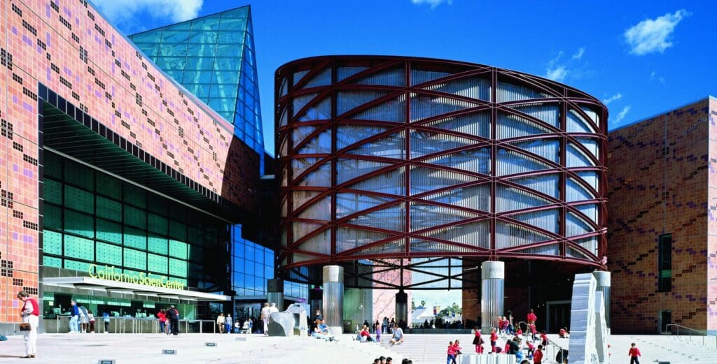 Modern architectural structure with cylindrical glass facade and patterned tiles; people on steps.