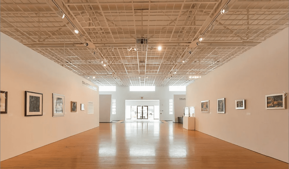 Modern art gallery with white walls, wooden floors, framed artworks, sculptures, and spacious layout.