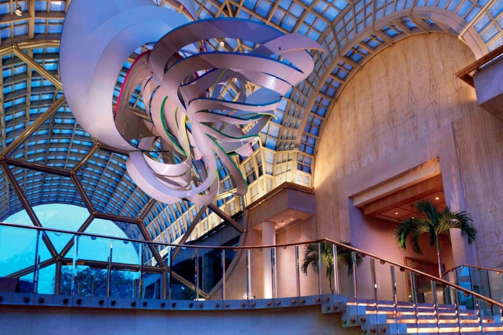 Modern atrium with abstract art, curved staircase, glass ceiling, and indoor plants.