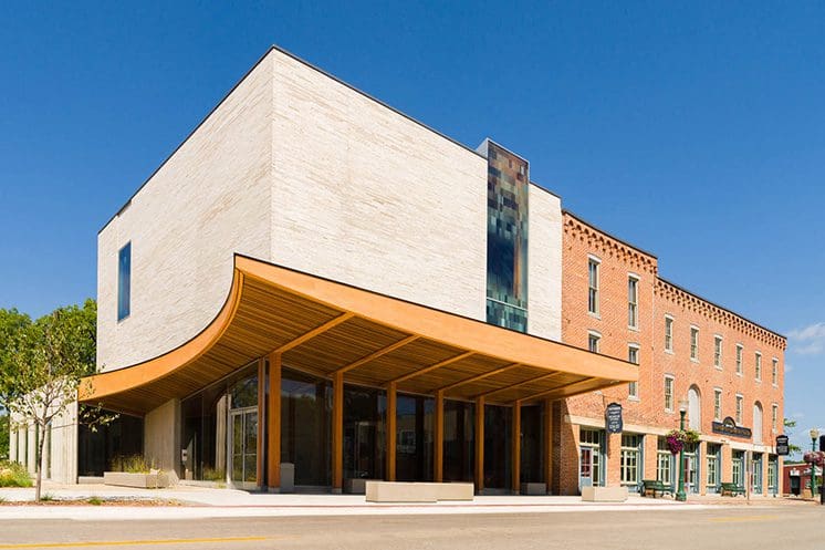 Modern beige building with wood overhang next to traditional brick buildings, glass windows, storefronts.