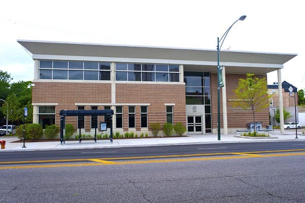 Modern two-story brick building with large windows, bus stop, and well-maintained urban surroundings.