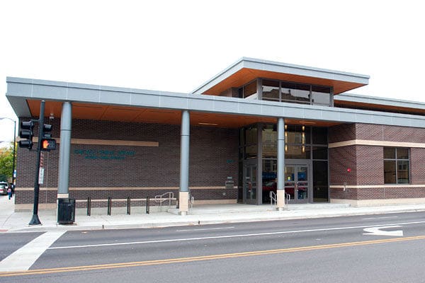 Modern brick building with flat roof, large glass entrance, pillars, windows, street, crosswalk, traffic light