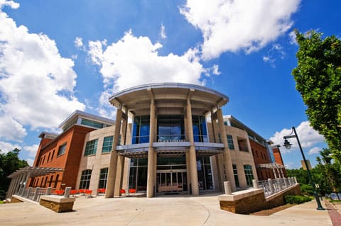 Modern multi-story brick and glass building with columns and overhang, set against a clear sky.