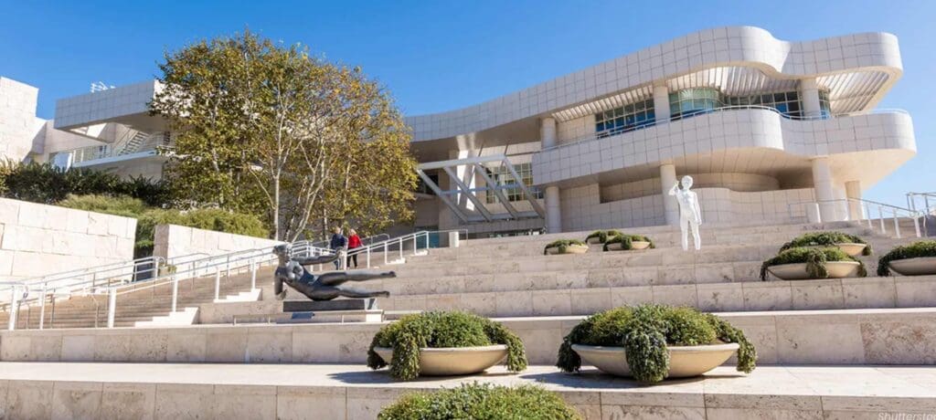 Modern building with curved facade, stairway, sculptures, landscaped planters, people, and clear sky